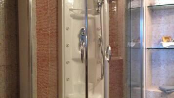 A glass-enclosed shower stall with a white toilet and a glass shelf to the right.