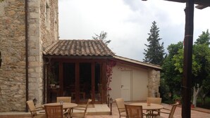 A stone building with a tiled roof and a covered patio area with wicker furniture. - Pyrgos Of Mystra (Sparta)