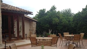 An outdoor patio with a round table and wicker chairs, surrounded by a stone wall and greenery. - Pyrgos Of Mystra (Sparta)