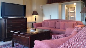 A living room with a television on a wooden cabinet, a sofa, a coffee table, and a lamp. - Pyrgos Of Mystra (Sparta)