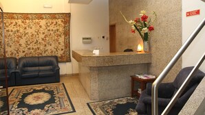 Un área de recepción con un mostrador de piedra, un florero con flores, un sofá y una alfombra estampada.