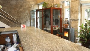 Un hall de hotel con pared de piedra, una mesa de recepción, una vitrina de madera y una estufa de leña.