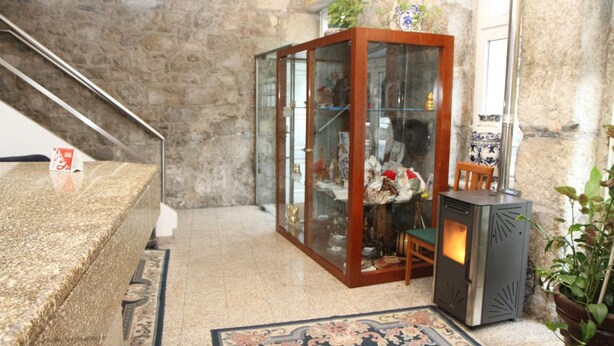 Una habitación con pared de piedra, un mueble de madera con puertas de cristal, una mesita y una planta en maceta.