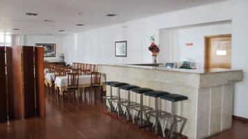 Une salle à manger d’hôtel avec une longue table et des chaises, un bar avec des tabourets et un comptoir agrémenté d’un vase de fleurs.