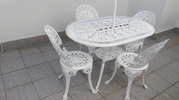 Una mesa blanca para exteriores y cuatro sillas a juego con diseños elaborados, sobre un suelo de baldosas.
