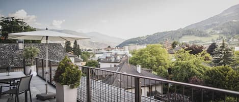 A terrace with a table and chairs, a potted plant, and a view of a town and mountains.
