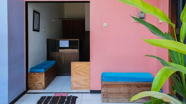 A reception area with a sign, wooden benches, and a plant. - Reddoorz Syariah Near Rsud Tuban (Tuban)