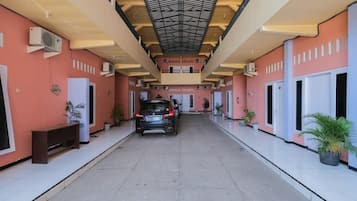 A covered corridor with a car parked at the end, air conditioning units on the walls, and potted plants along the sides.