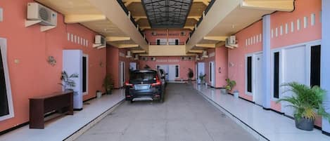 A covered corridor with a car parked at the end, air conditioning units on the walls, and potted plants along the sides.