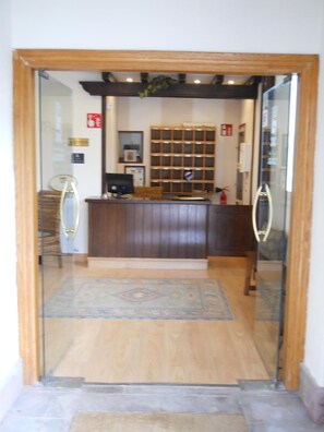 A reception area with a wooden reception desk, a computer monitor, and a patterned rug. - Hotel Elizondo (Baztan)