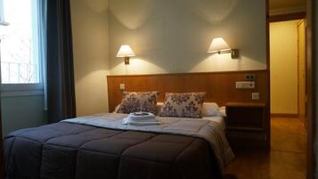 Habitación de hotel con cama, dos lámparas de pared, una mesita de noche y una ventana.