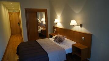 Habitación de hotel con cama, lámparas de noche, cabecero de madera y una puerta con la leyenda 'SALIDA'.