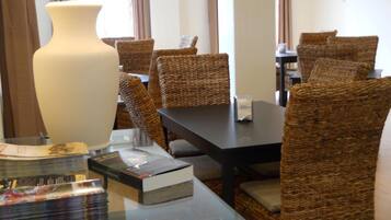 Un comedor de hotel con sillas de mimbre, una mesa de vidrio y una lámpara grande.