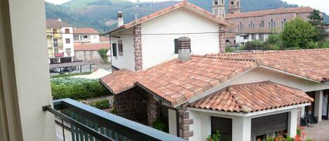 A residential area with terracotta-tiled roofs, a church with a bell tower, and a hillside in the background.