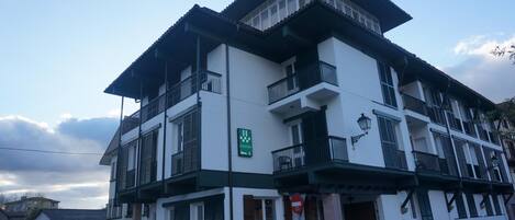 Un immeuble à plusieurs étages doté de balcons, une enseigne bien visible indiquant qu’il s’agit d’un hôtel, et des voitures garées au premier plan.