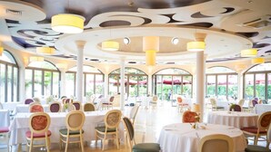 A restaurant with round tables and chairs, large windows, and a ceiling with circular patterns. - Hotel Park Central (Sliven)