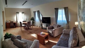 A living room with a sofa set, a coffee table, a TV, and a dining area with chairs and a table. - Hotel Park Central (Sliven)