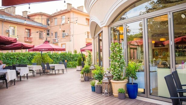 An outdoor patio area with tables and chairs, potted plants, and umbrellas. - Hotel Park Central (Sliven)