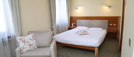 Habitación de hotel con cama, una silla, mesita de noche y lámpara de pared.
