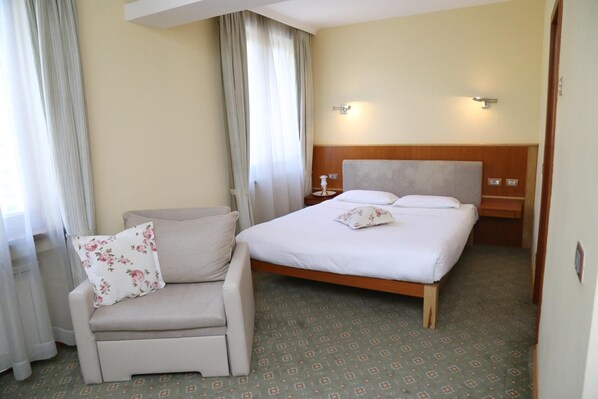 A hotel room with a bed, a chair, a nightstand, and a wall-mounted lamp. - Hotel Park Central (Sliven)