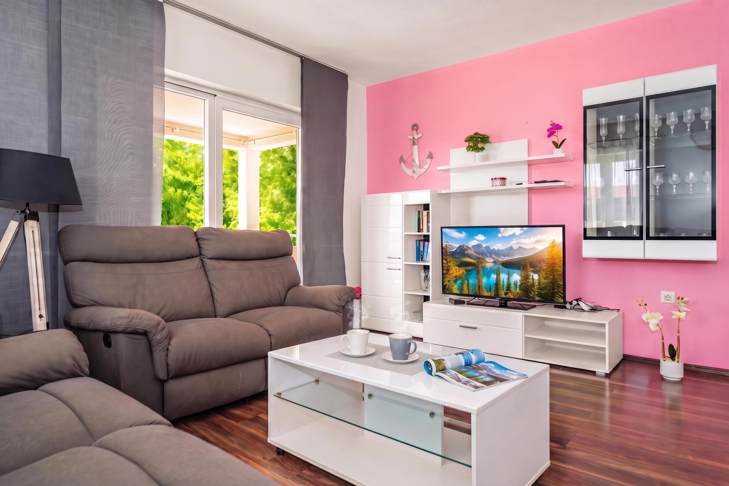 Ein modernes Wohnzimmer mit einer Couch, einem Couchtisch, einem Fernseher und einer rosafarbenen Wand.