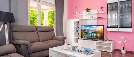Ein modernes Wohnzimmer mit einer Couch, einem Couchtisch, einem Fernseher und einer rosafarbenen Wand.
