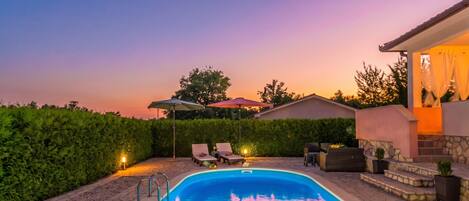 A swimming pool with lounge chairs and umbrellas, surrounded by a stone patio and a hedge.