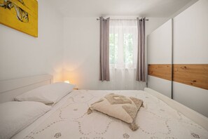 Ein Schlafzimmer mit einem Bett, einem Nachttisch, einem Fenster mit Vorhängen und einem hölzernen Kopfteil.