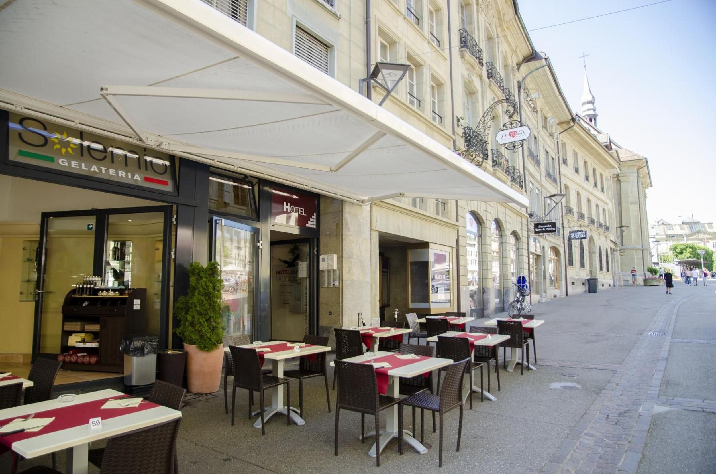 Un café al aire libre con mesas y sillas, una heladería al otro lado de la calle y un edificio con balcón.