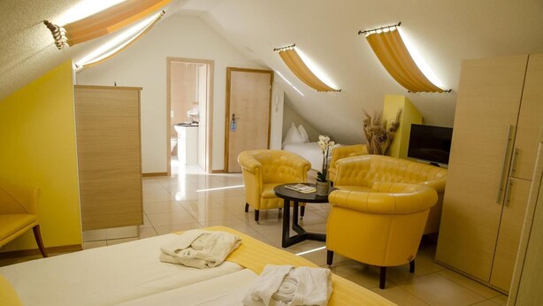 A hotel room with a bed, two armchairs, a small table, and a TV. - Hotel Du Faucon (Fribourg)