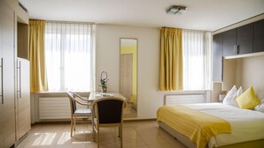A hotel room with a bed, a desk, a chair, a mirror, and a wardrobe. - Hotel Du Faucon (Fribourg)
