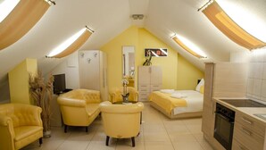 A compact room with a bed, two armchairs, a small table, a cabinet, a television, and a kitchenette. - Hotel Du Faucon (Fribourg)