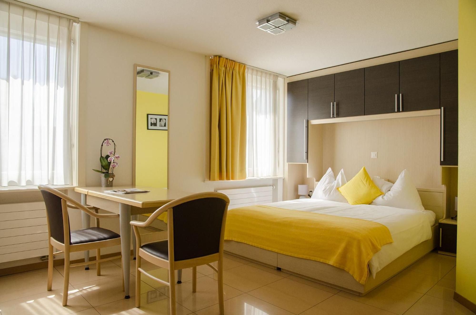 A hotel room with a bed, a desk, two chairs, a mirror, and a window with curtains.