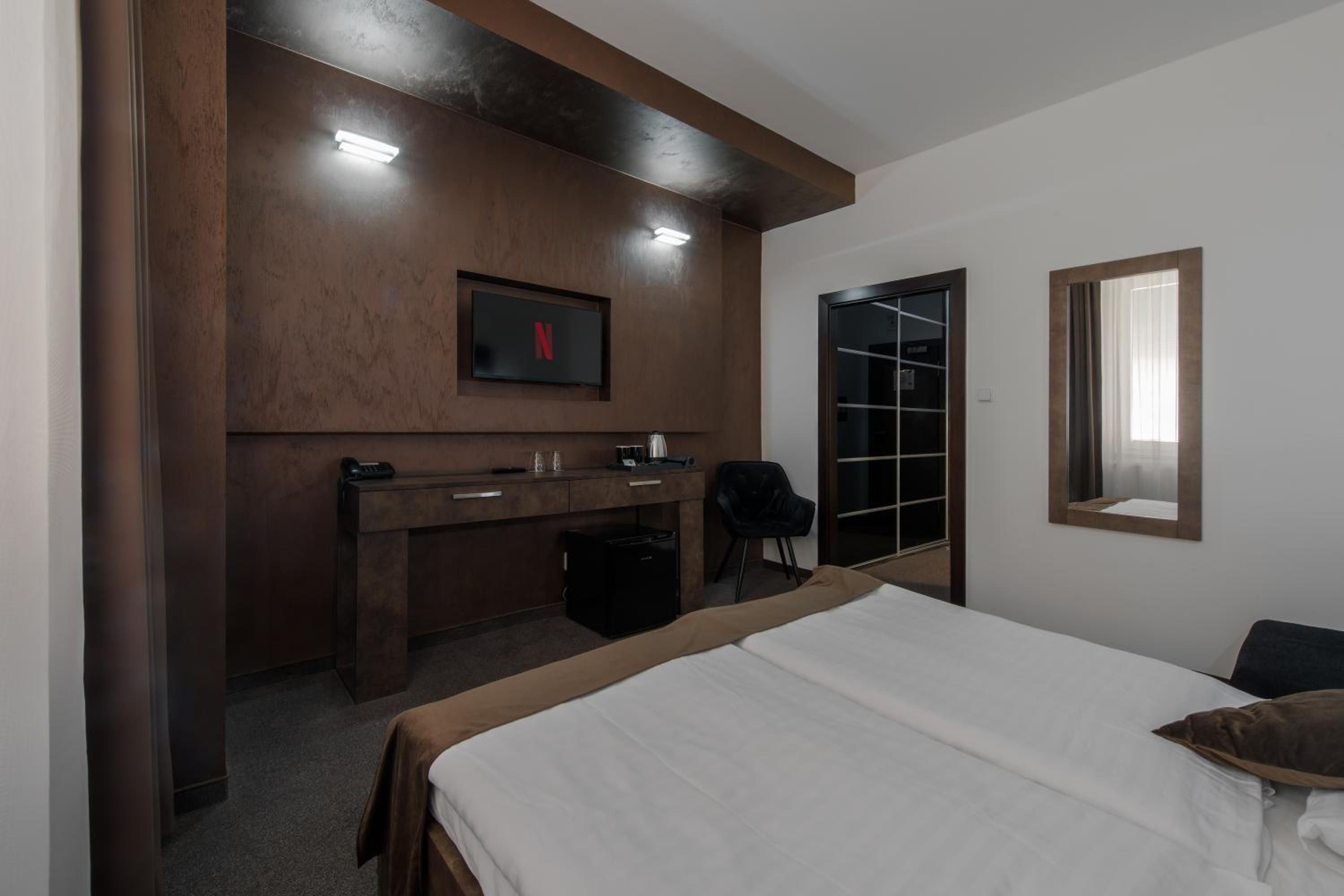 A hotel room with a bed, a desk with a chair, a TV mounted on the wall, and a door leading to a closet.