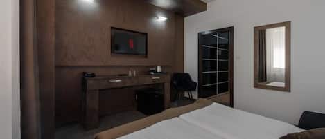 Habitación de hotel con cama, escritorio con silla, televisor montado en la pared y puerta que da a un armario.