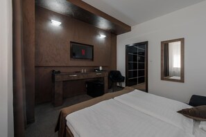 A hotel room with a bed, a desk with a chair, a TV mounted on the wall, and a door leading to a closet. - Hotel Polo (Prešov)
