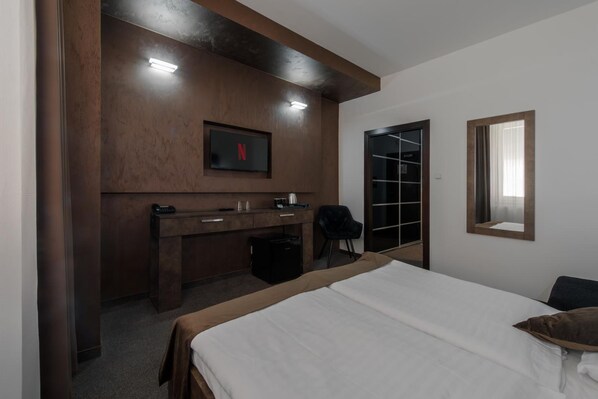A hotel room with a bed, a desk with a chair, a TV mounted on the wall, and a door leading to a closet. - Hotel Polo (Prešov)
