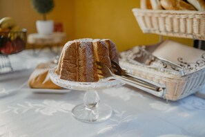 A cake on a glass stand with a fork, a basket of bread, and a small potted plant in the background. - Hotel Polo (Prešov)
