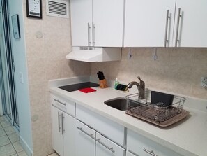 Una cucina con mobili bianchi, un lavello in acciaio inossidabile, un espositore per piatti e un tagliere rosso.