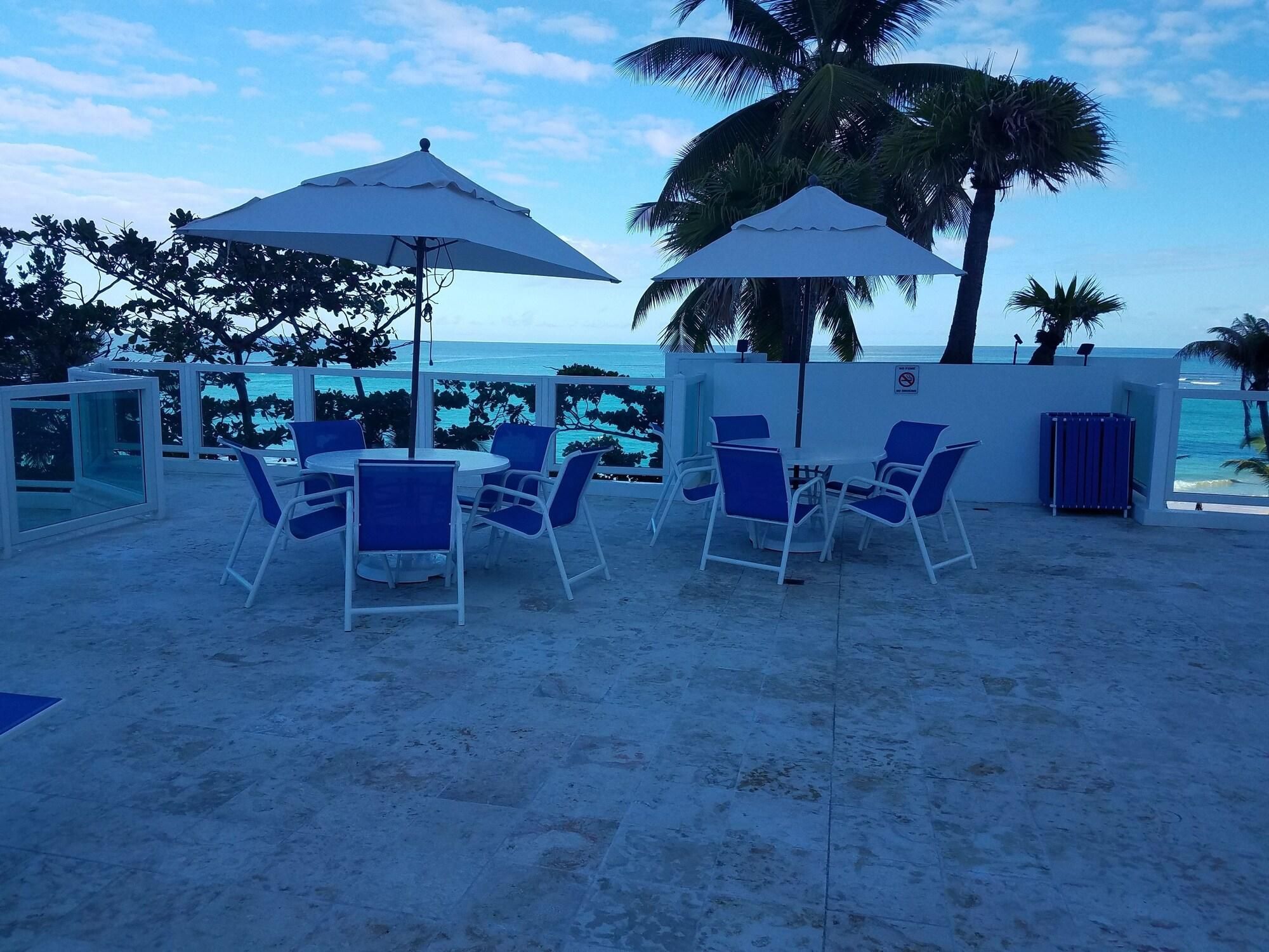 Un patio frente a la playa con mesas, sillas, sombrillas y vista al océano.