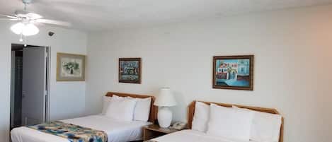 Una habitación de hotel con dos camas, un ventilador de techo, una puerta y dos cuadros en la pared.