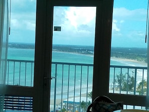 Vista desde un balcón con barandilla, sobre una playa y el océano.