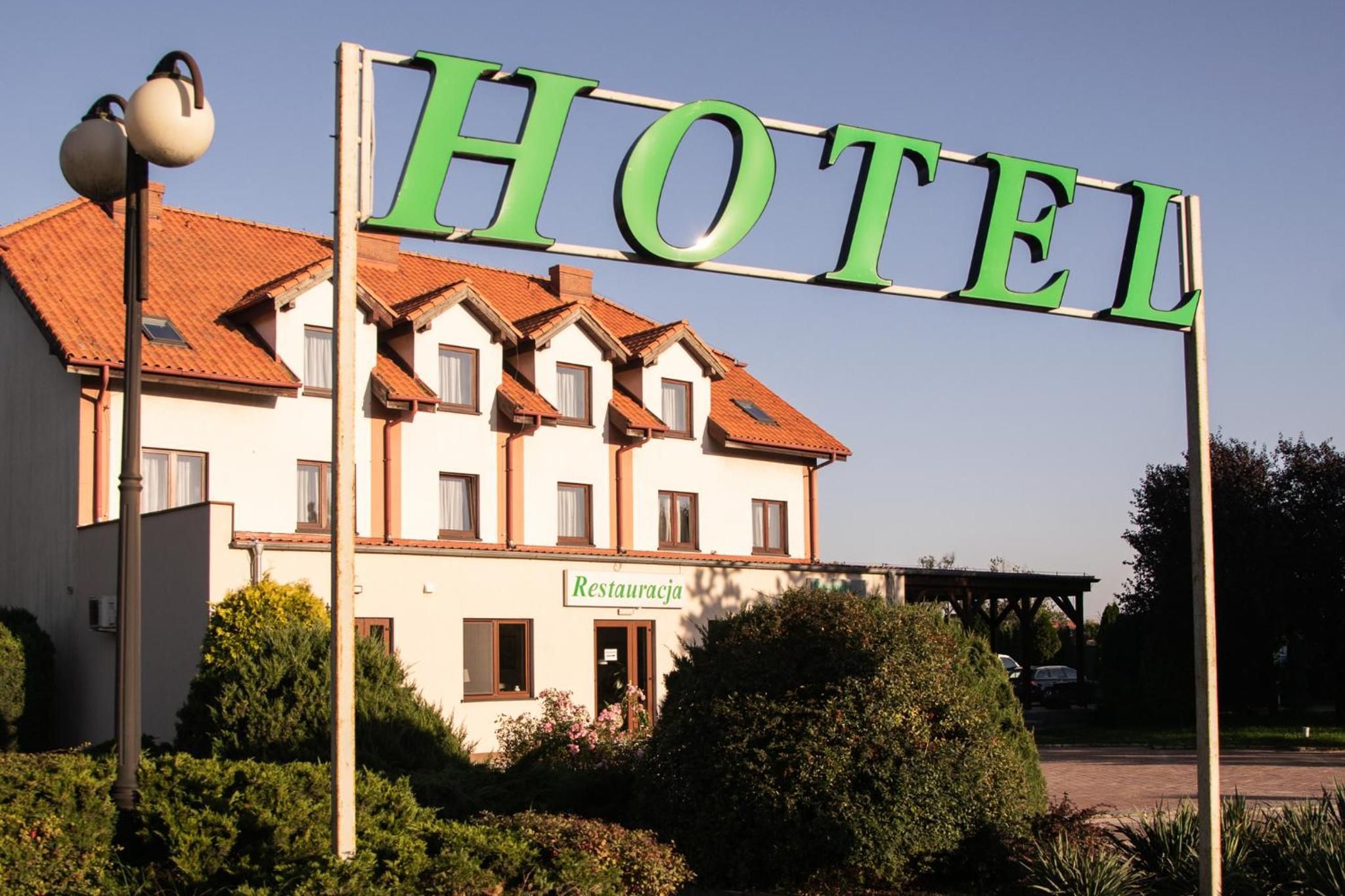 Ein Hotel mit auffälligem, grünem Schild, einem roten Ziegeldach und einem Hinweis auf ein Restaurant im Erdgeschoss.