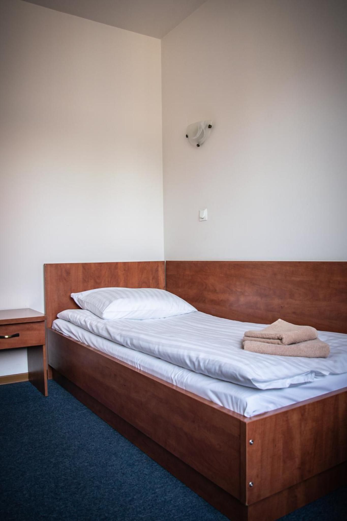 Ein Einzelbett mit Holz-Kopfteil, ein Nachttisch und eine Wandleuchte.