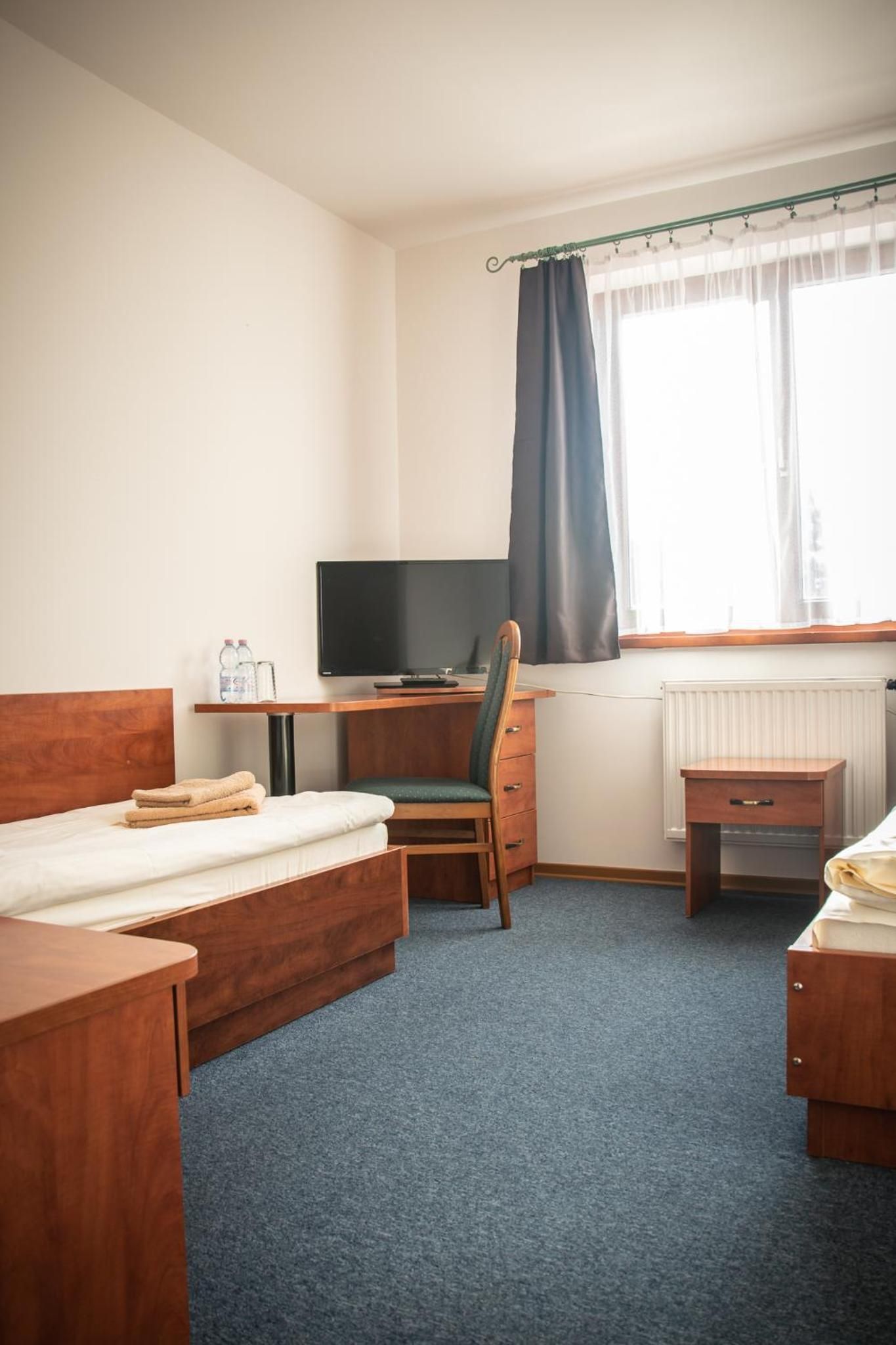 Ein Hotelzimmer mit Bett, Schreibtisch mit Computer, Stuhl, einem kleinen Tisch und einem Heizkörper.