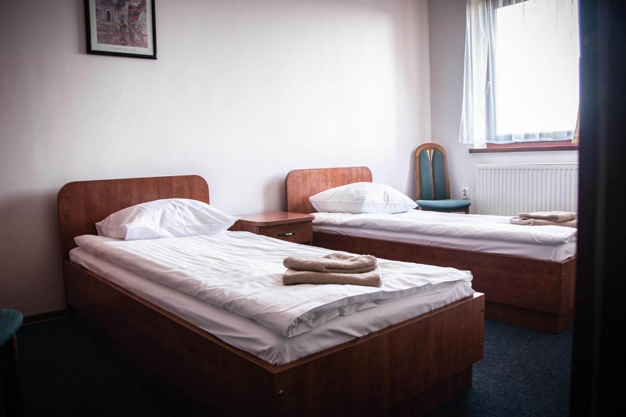 Ein Hotelzimmer mit zwei hölzernen Betten, weißer Bettwäsche, einem Sessel, einem kleinen Tisch und einem fenster mit Vorhängen.