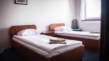 A hotel room with two wooden beds, white bedding, a chair, a small table, and a window with curtains.