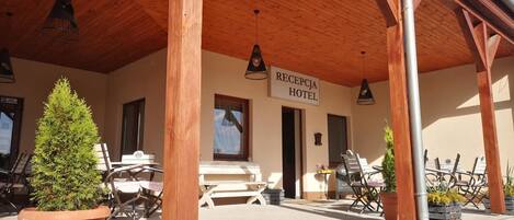 A hotel reception area with a wooden ceiling, outdoor seating, and a sign indicating it's a hotel.