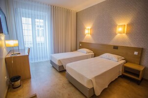 A hotel room with two beds, a desk, a chair, a lamp, and a window with curtains.
