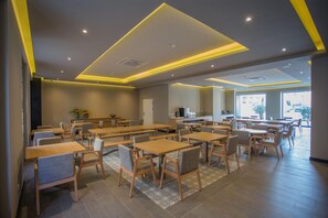 A modern dining area with multiple tables and chairs, a kitchen in the background, and a patterned rug on the floor. - Hotel Brazv O (Vila do Conde)